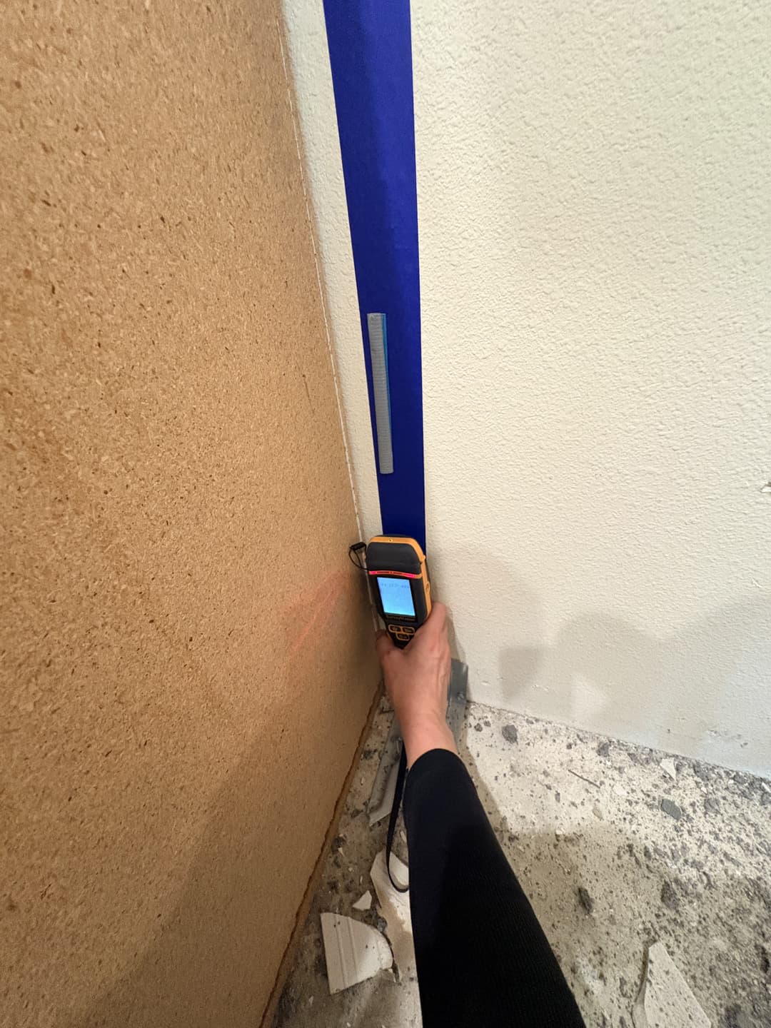 Digital moisture meter measuring saturation levels on drywall near plumbing wall in Anaheim residence