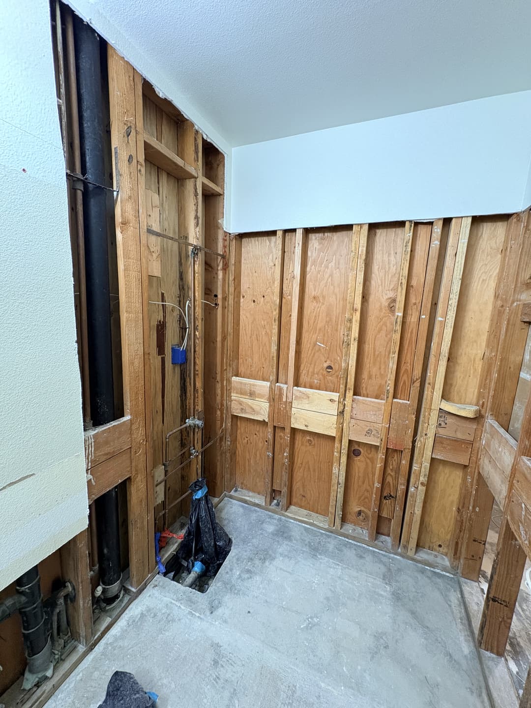Full drywall removal in bathroom exposing studs and drain pipe after water damage at Anaheim property