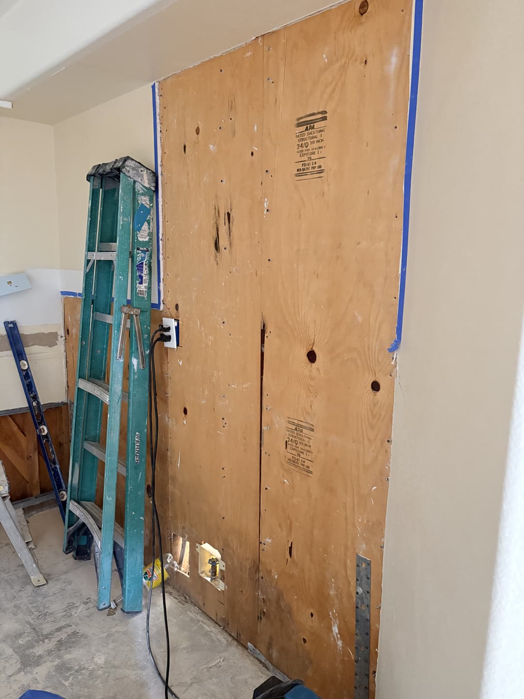 Plywood wall sheathing with blue painter's tape edging visible after drywall removal in Anaheim kitchen