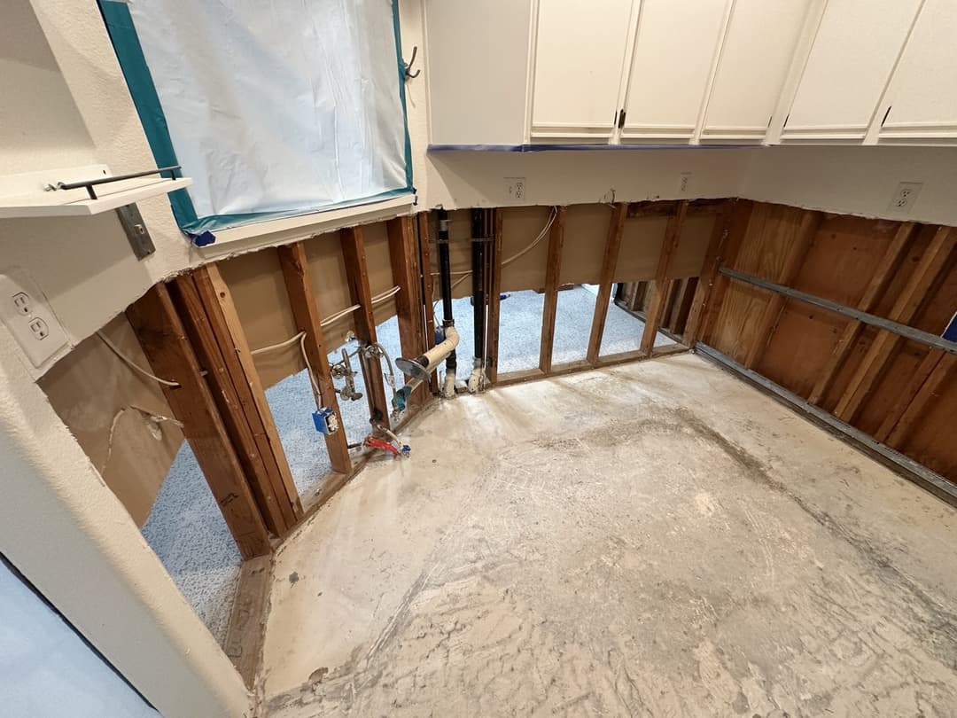 Kitchen demolition in progress with tile removal, exposed subfloor, and blue tape marking containment lines in Anaheim