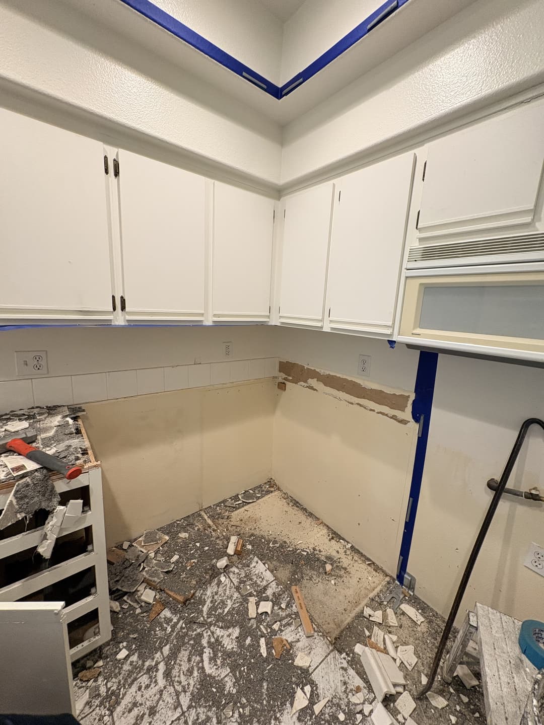 Kitchen walls with drywall removed below upper cabinets exposing studs and plumbing after water damage in Anaheim